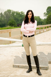 Front view of a female model wearing the beige KL Select Gabrielle Breech while standing in an outdoor arena