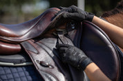 View of a model attaching a brown Total Saddle Fit Slim Stability Stirrup Leather to a brown jump saddle on a horse