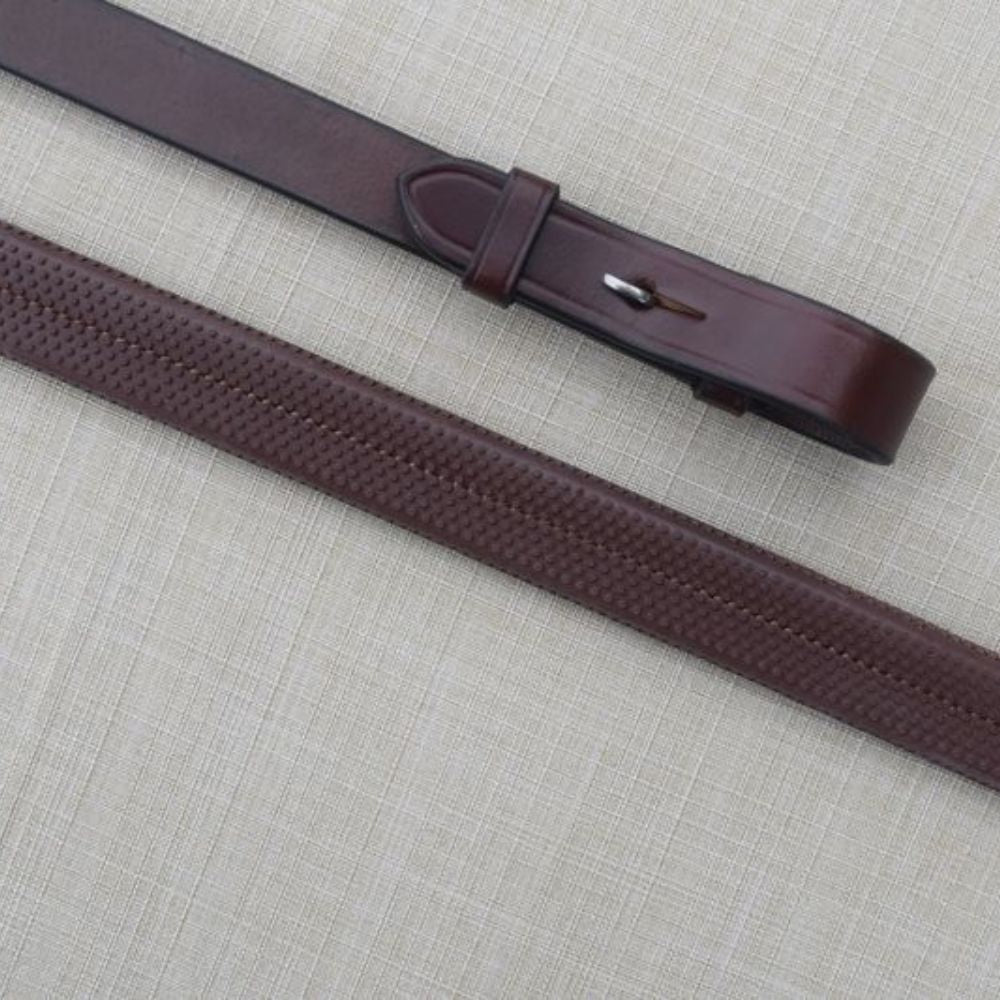 A dark brown leather reins with a textured rubber pattern on the strap and a polished silver-tone buckle, laid diagonally on a light beige linen background.