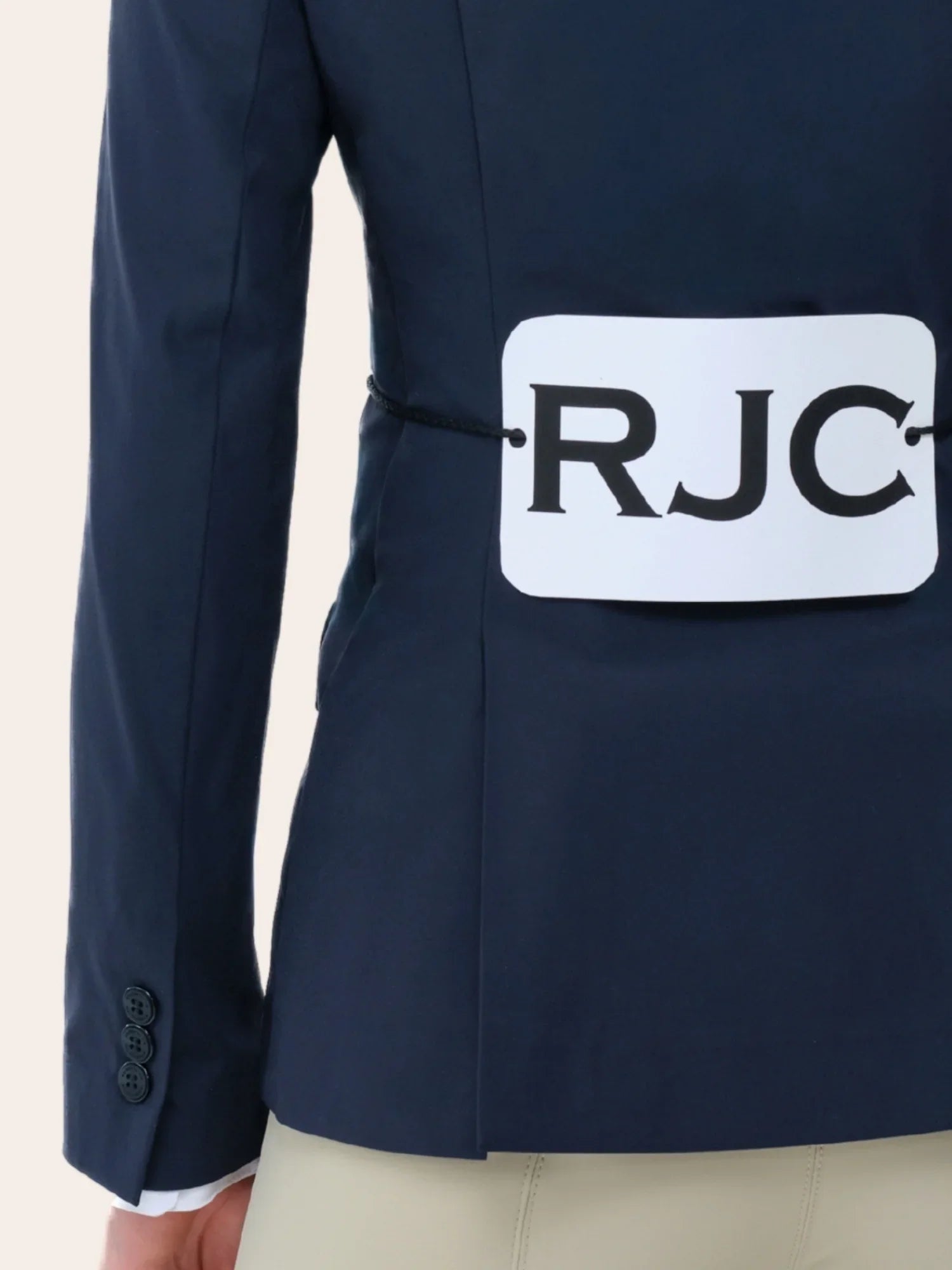 Close-up back view of a young female model wearing the navy RJ Classics Legacy Lite Jr Show Coat with RJC competition number tabard on a plain background