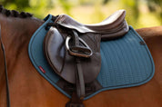 Close up of a gray horse wearing the LeMieux Essence Close Contact Square in blue-green under a brown saddle