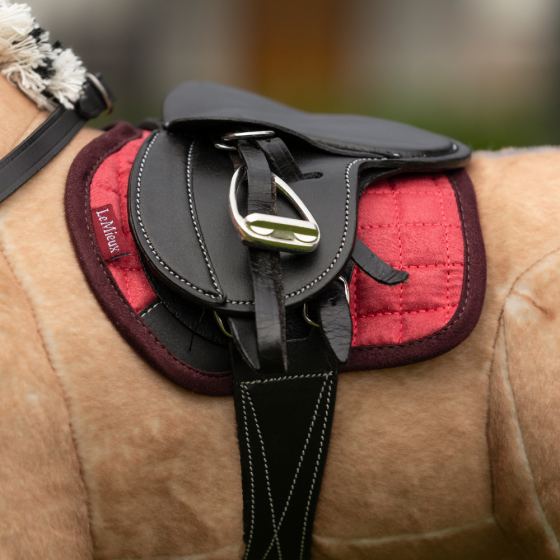Close-up view of the cranberry LeMieux Toy Pony Saddle Pad under a black saddle