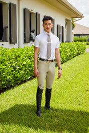 Man standing outside a stable while wearing the white RJ Classics Tyler Show Shirt, tan tie. tan breeches, and black tall boots