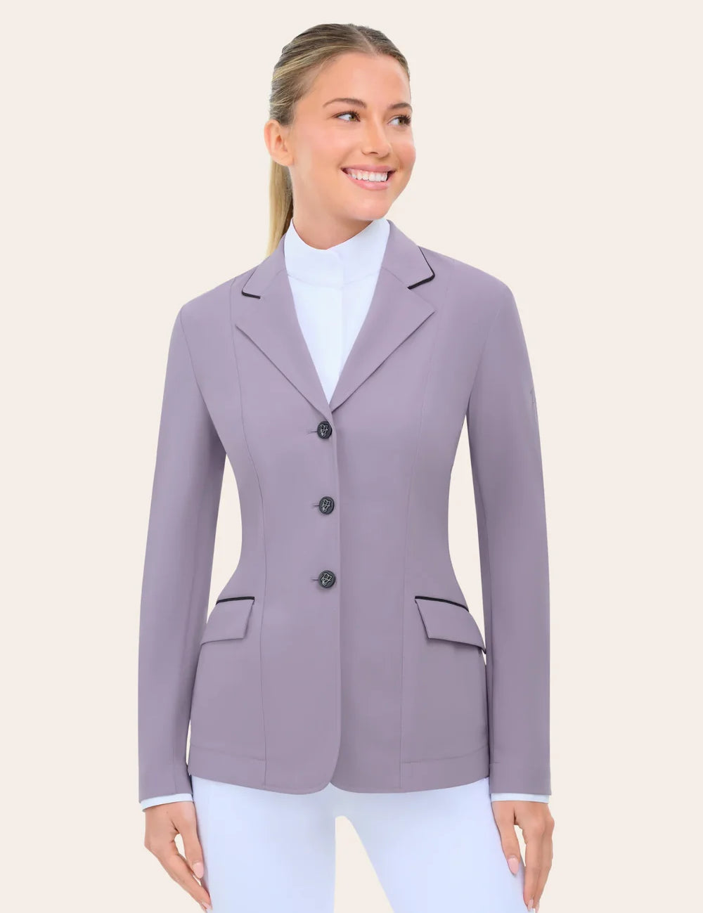 Angled front view of the RJ Classics Monterey Show Coat Eleganza Edition in Dusty Lilac, a tailored equestrian show jacket with notched lapel and contrast piping, three-button front closure, and flap pockets, shown on a model over a white high-collar show shirt and white riding breeches against a plain light background.