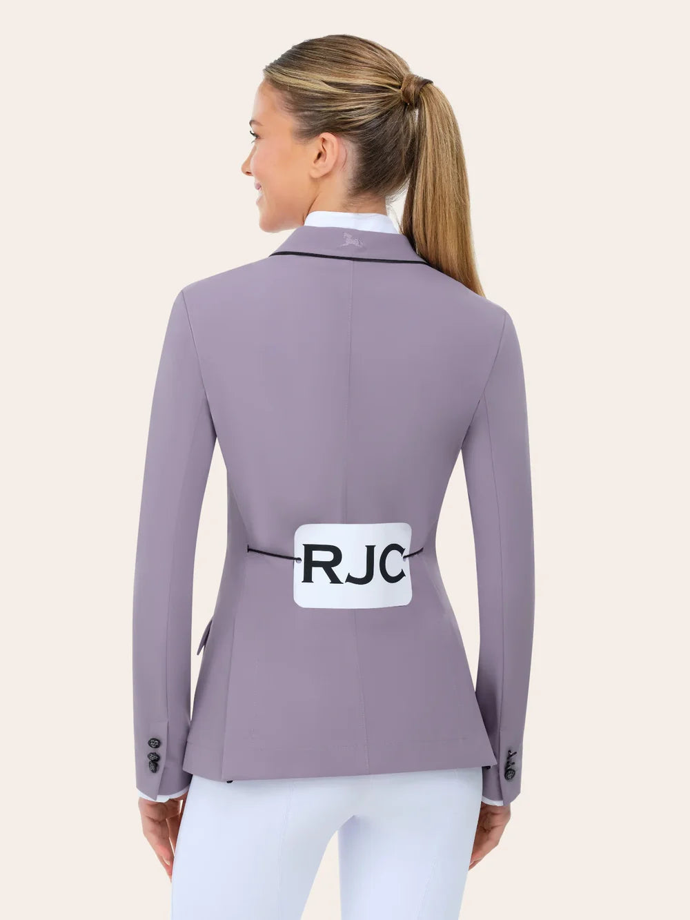 Back view of the RJ Classics Monterey Show Coat Eleganza Edition in Dusty Lilac, a fitted equestrian show jacket with black collar piping, center back seam, and buttoned cuffs, shown over a white show shirt and white riding breeches on a model against a plain light background.