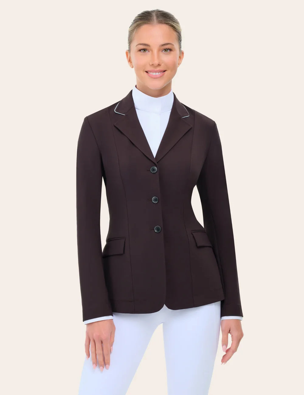 Front view of the RJ Classics Monterey Show Coat in fig, a tailored equestrian show jacket with notched lapel and contrast piping, three-button front closure, and flap pockets, shown on a model over a white high-collar show shirt and white riding breeches against a plain light background.
