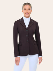Front view of the RJ Classics Monterey Show Coat in fig, a tailored equestrian show jacket with notched lapel and contrast piping, three-button front closure, and flap pockets, shown on a model over a white high-collar show shirt and white riding breeches against a plain light background.