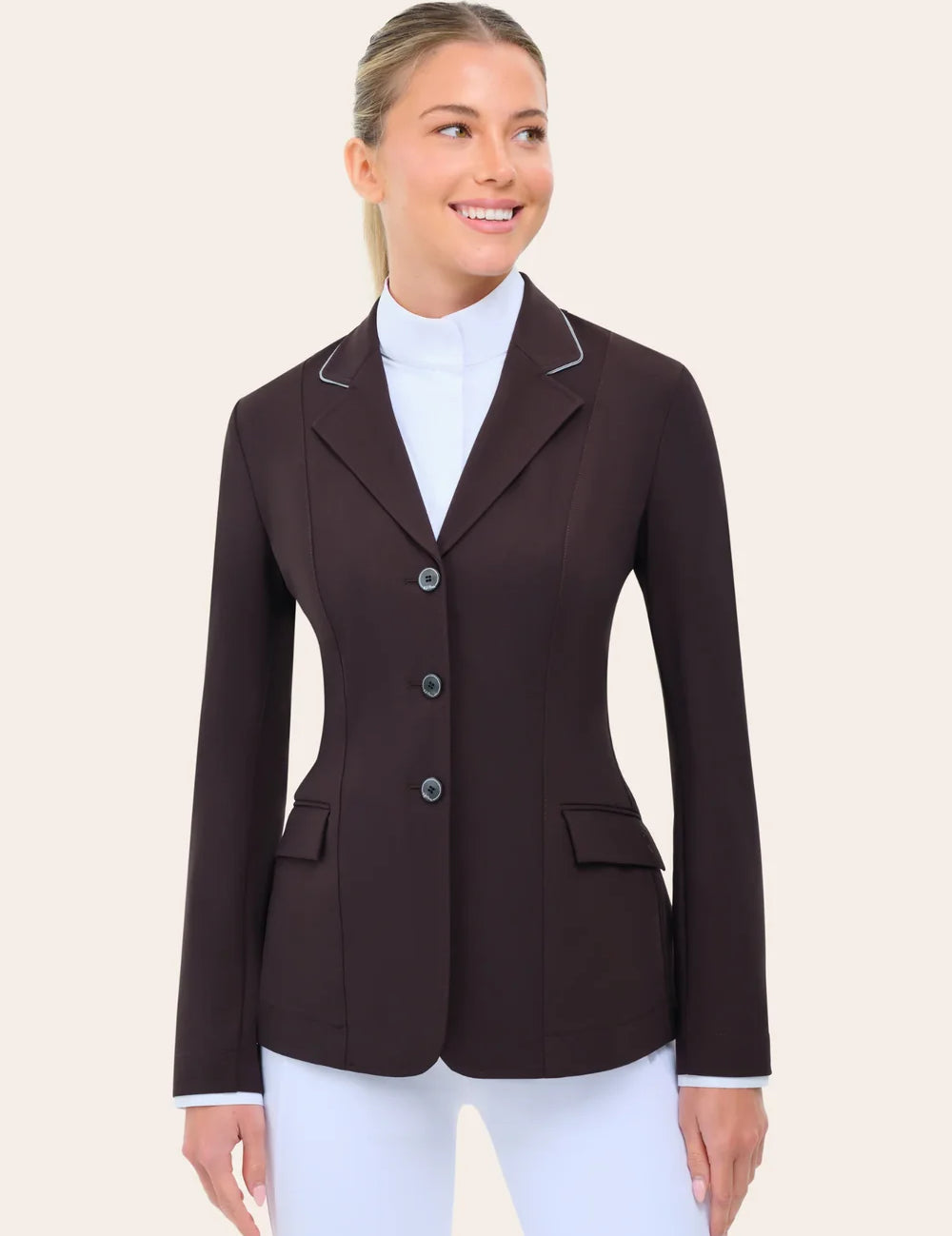 Angled front view of the RJ Classics Monterey Show Coat in fig, a fitted equestrian show jacket with notched lapel and contrast piping, three-button front closure, and flap pockets, shown over a white high-collar show shirt and white riding breeches against a plain light background.