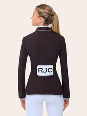 Back view of the RJ Classics Monterey Show Coat in fig, a fitted equestrian show jacket with a smooth tailored finish, contrast piping along the collar, center back seam, and buttoned cuffs, shown on a model over a white show shirt and white riding breeches against a plain light background.