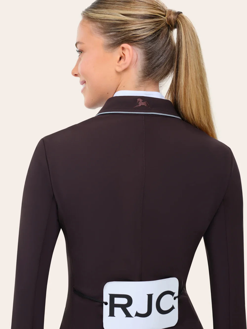 Back-detail view of the RJ Classics Monterey Show Coat in fig featuring a smooth tailored fit, contrast piping along the collar, and an embroidered logo at the back neck, shown over a white show shirt on a model against a plain light background.