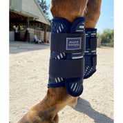 Side view of a horse wearing the navy and silver tendon boots from the Majyk Equipe XC Elite 4 Pack while standing in the dirt outside