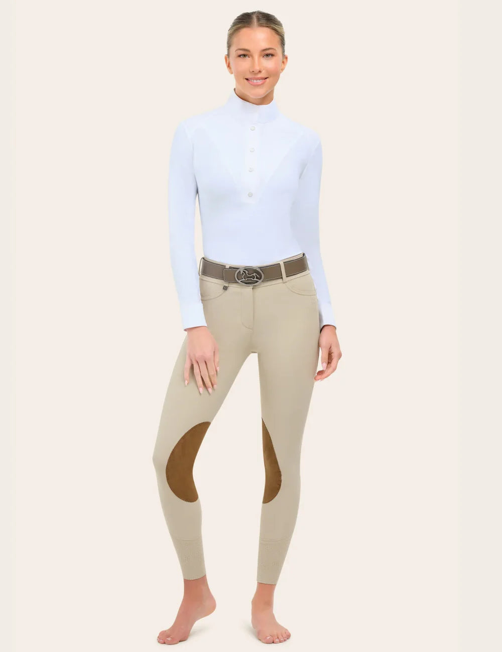 Full-length view of the RJ Classics Olivia Luxe-Tek Breech in Sand, featuring a double-button waistband with belt loops, smooth stretch fabric, brown suede knee patches, and perforated lower-leg panels, shown on a model wearing a white long-sleeve show shirt against a plain light background.