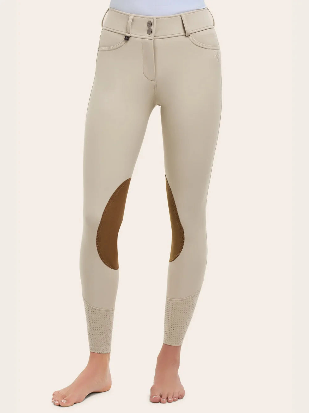 Angled front view of the RJ Classics Olivia Luxe-Tek Breech in Sand, showing the double-button waistband with belt loops, smooth stretch fabric, brown suede knee patches, and perforated lower-leg panels, photographed on a model against a plain light background.