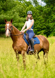 Side view of a female model riding a chestnut horse that is wearing the Nightfall Kerrits Close Contact Saddle Pad while standing in a field of tall grass
