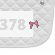 Side view of a white pad with numbers 378 and a Pink Bow Dubois Cheval Number Pin Charm on a white background
