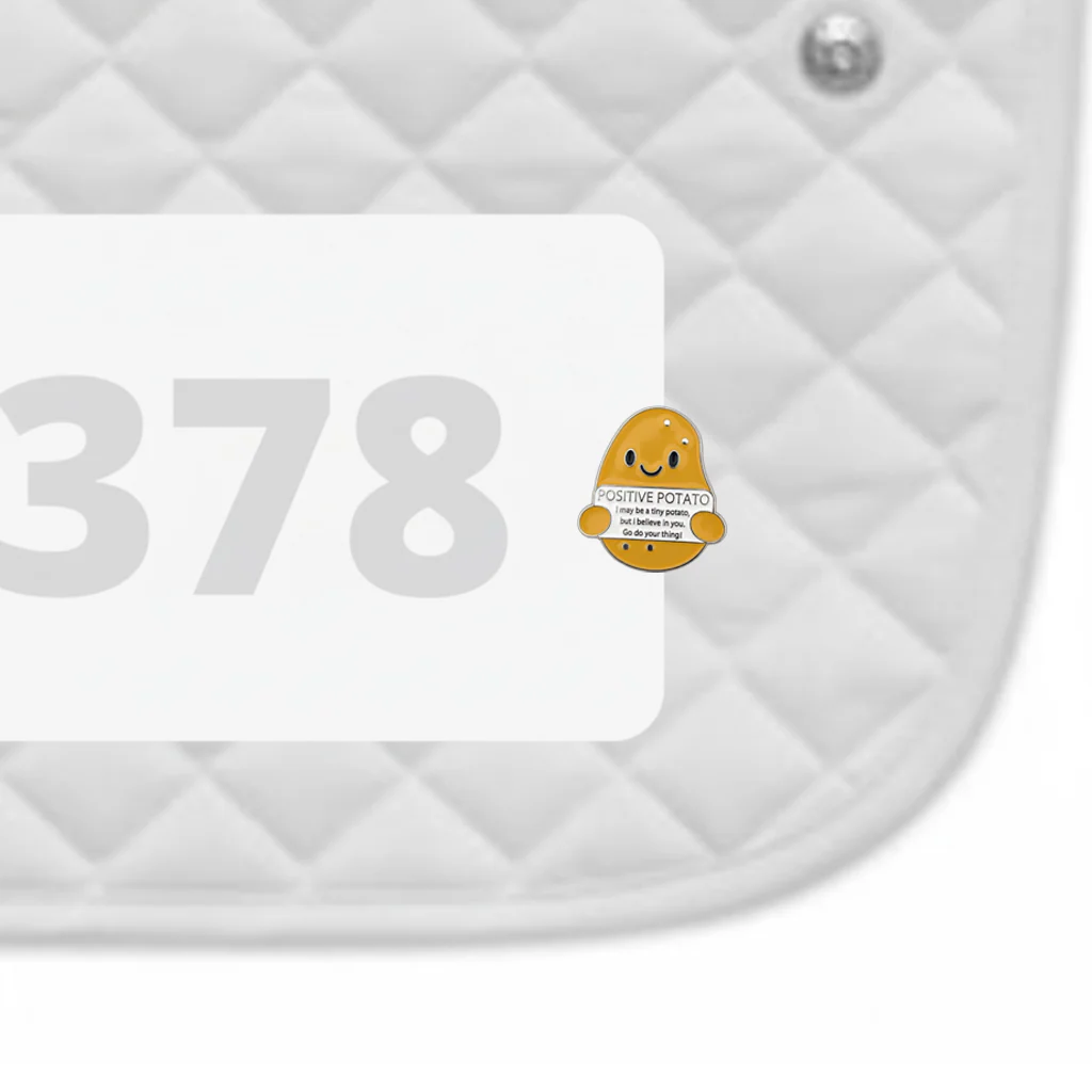 Side view of a white pad with numbers 378 and a Positive Potato Dubois Cheval Number Pin Charm on a white background