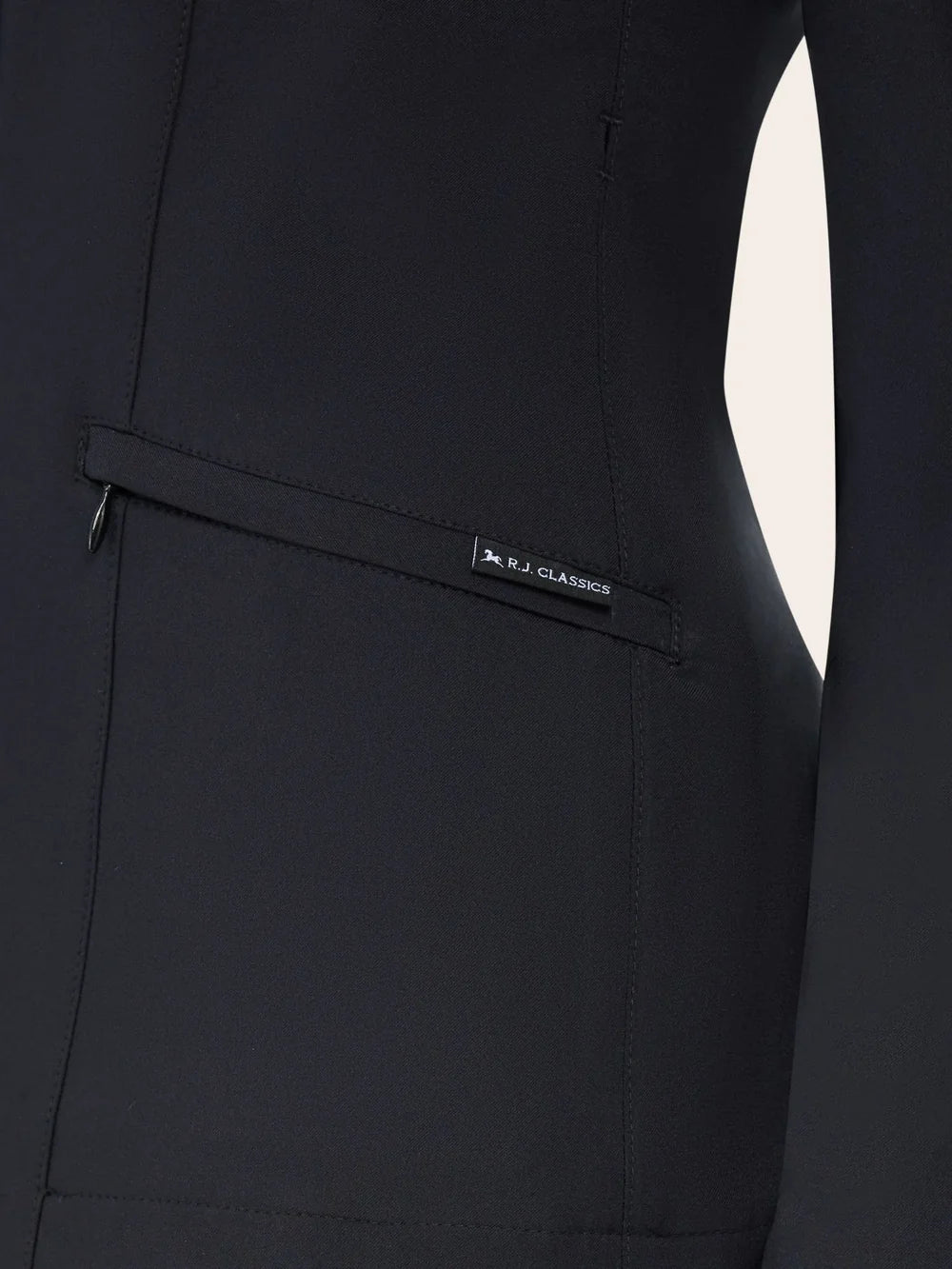 Close-up of the RJ Classics Sloane Show Coat in black showing a slanted zip pocket with an RJ Classics fabric tag and stitched seam lines on the jacket front.