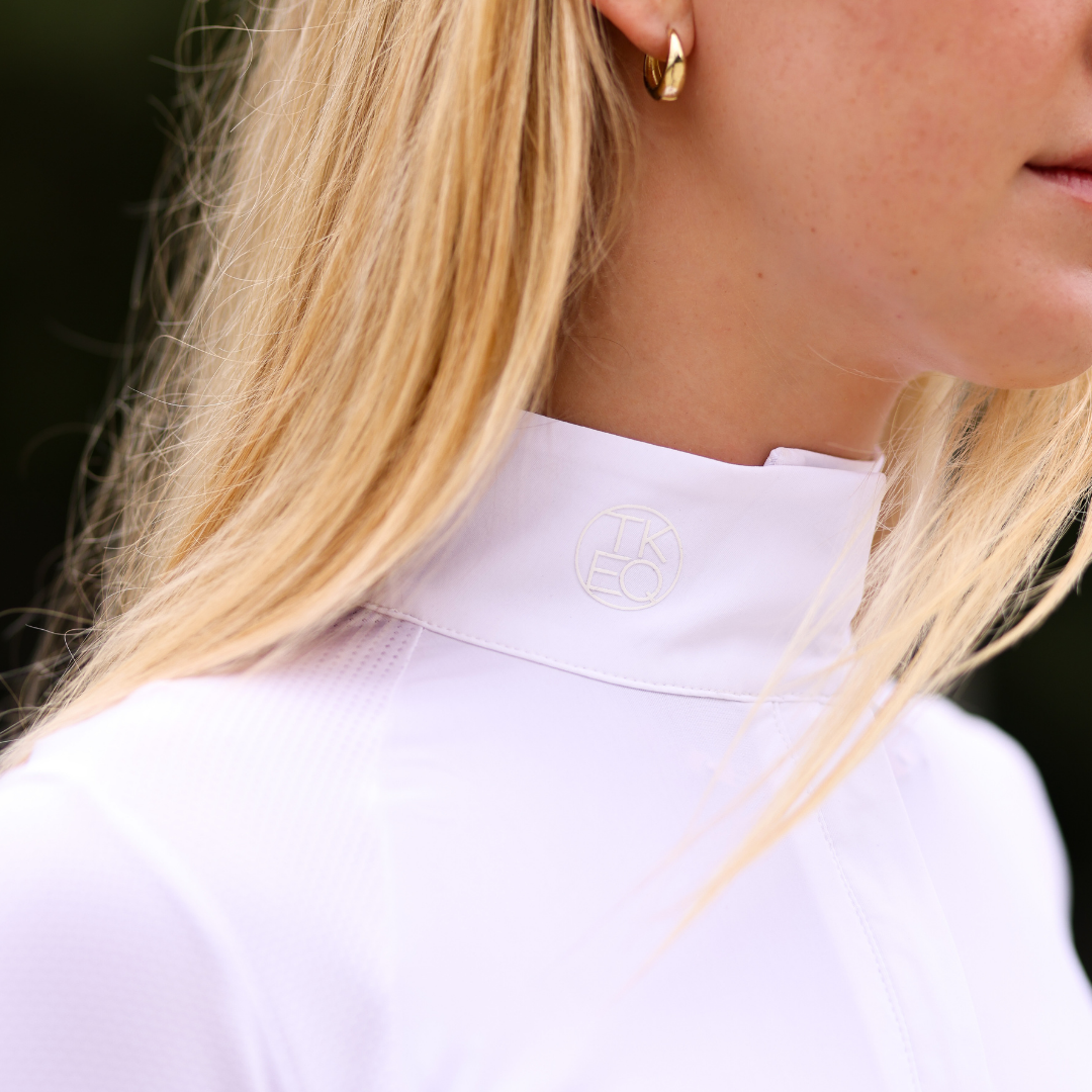 Close-up angled front view of a female model wearing the white TKEQ Sloan Competition Long Sleeve Top