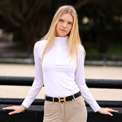 Front view of a female model wearing the white TKEQ Sloan Competition Long Sleeve Top while keaning up against  a black jump