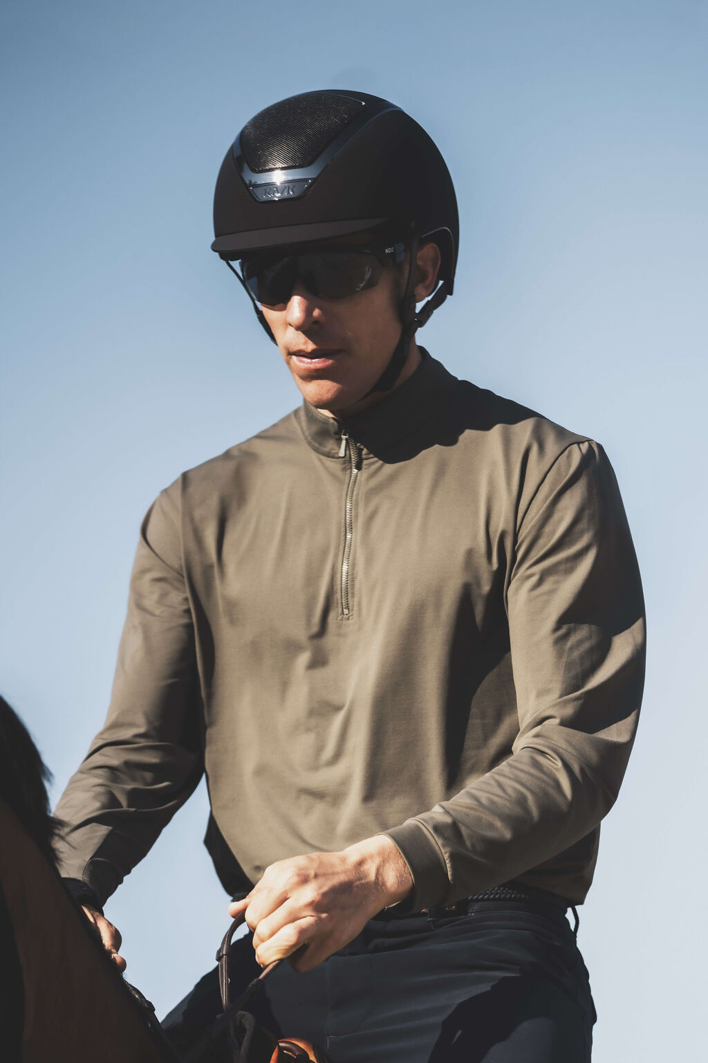 Angled front view of a male model wearing the black Kask Dogma Chrome Helmet while riding a horse