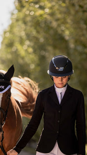Front view of a female model wearing the anthracite KASK Star Lady Chrome while leading a horse outside
