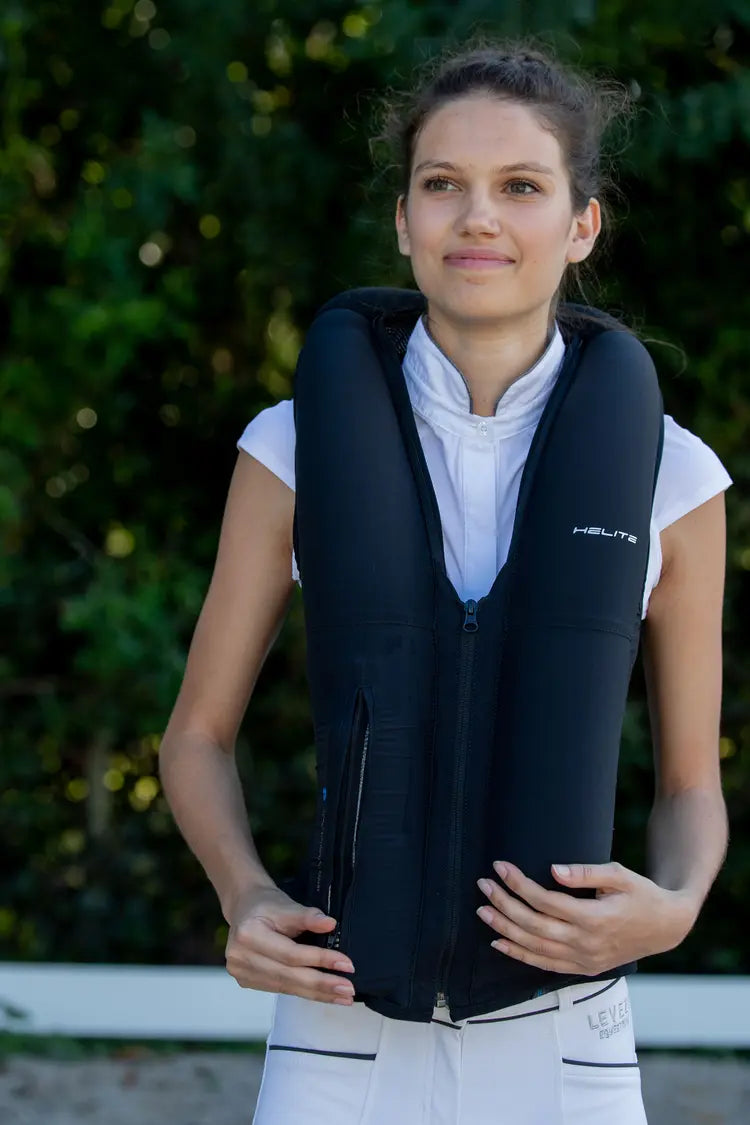 Model wearing the Helite Zip'In 2 Airbag in black with the airbags inflated, standing outside