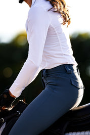 Side view of a model wearing the white Criniere Helen Show Shirt while riding a horse
