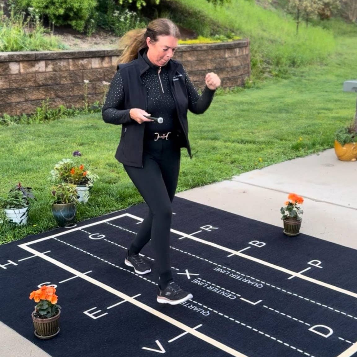 View of a model walking on the All Designs Equine Dressage Arena Practice Your Test Outdoor Horse Trainer Rug on an outdoor patio