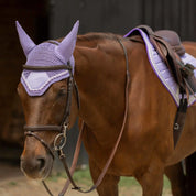 Angled front view of a horse wearing the purple Equinavia Copenhagen Ear Net and coordinating saddle pad under  brown tack