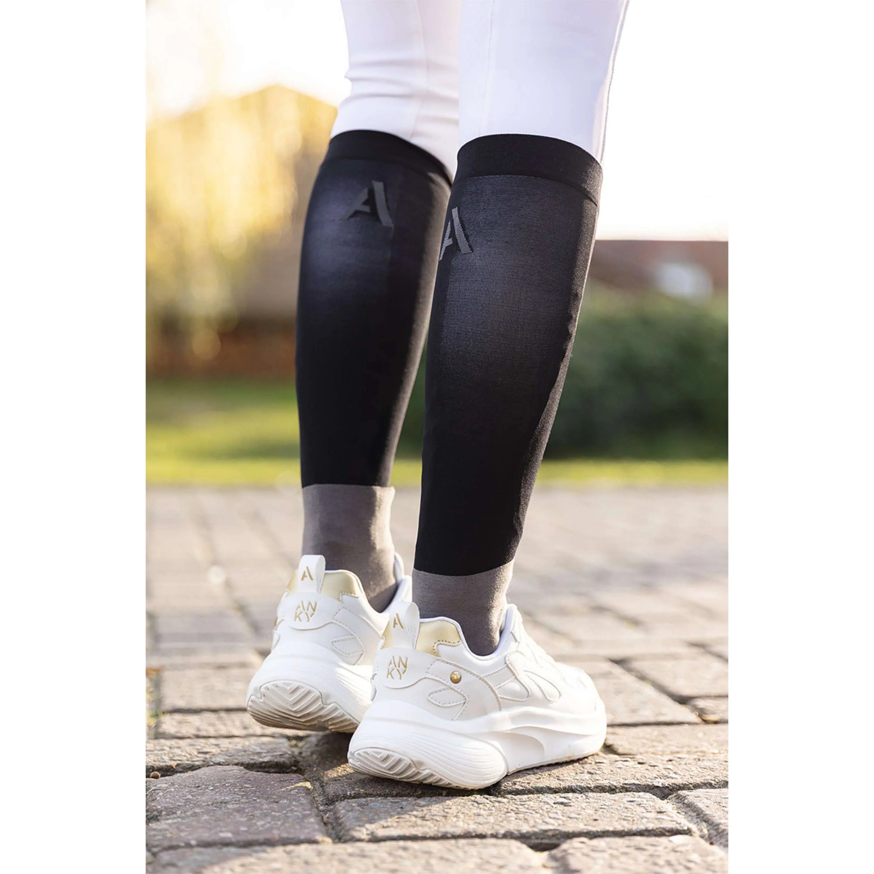 Back view of a model wearing the black ANKY Competition Socks while walking on a brick path outside