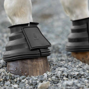 Black Equinavia Step Guard Rubber Bell Boots on a gray horse standing on gravel
