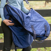Side view of a woman using the shoulder strap to carry a saddle in the navy Horze Saddle Bag