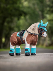 Angled front view of a paint toy pony wearing the azure LeMieux Toy Pony Saddle Pad while standing on a path outside