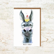 View of the More Cake Donkey Pony Nut Greeting Card on a white washed wood background