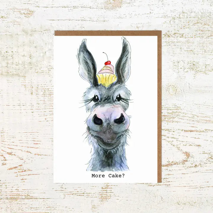 View of the More Cake Donkey Pony Nut Greeting Card on a white washed wood background
