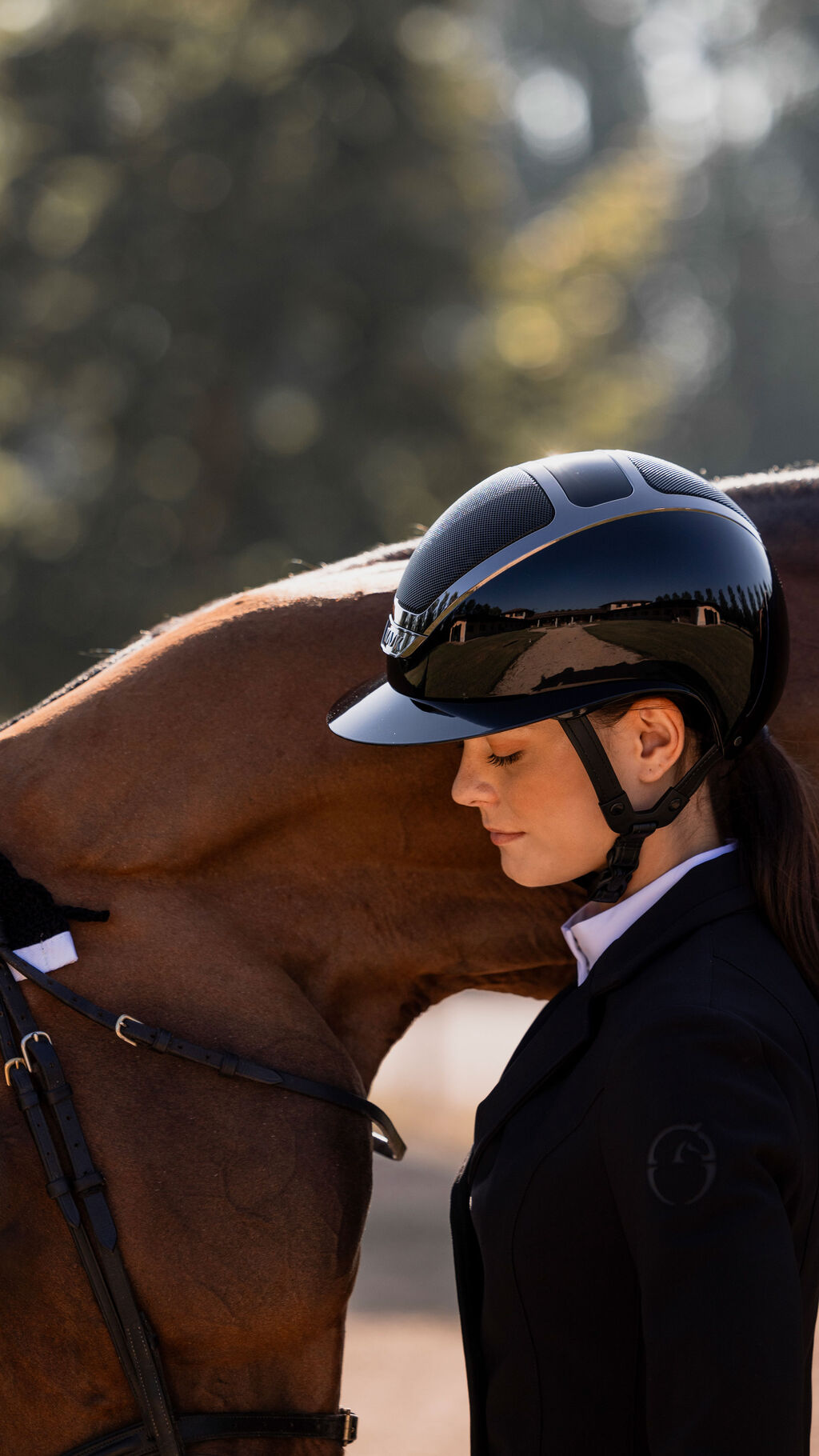 Side view of a female model wearing the black Star Lady Pure Shine Helmet while standing in front of a horse