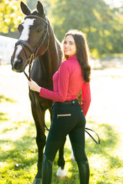 Full body back view of a female model wearing the black/cognac KL Select Gabrielle Knee Patch Breech while standing in front of a bay horse