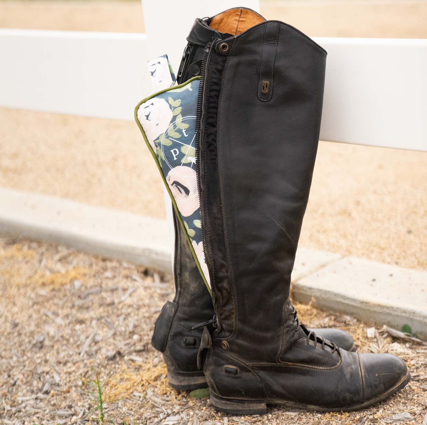 Side view of a pair of tall boots with a boot stuffer showing through the back zipper with a white fence in the background