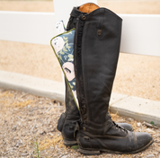 Side view of a pair of tall boots with a boot stuffer showing through the back zipper with a white fence in the background
