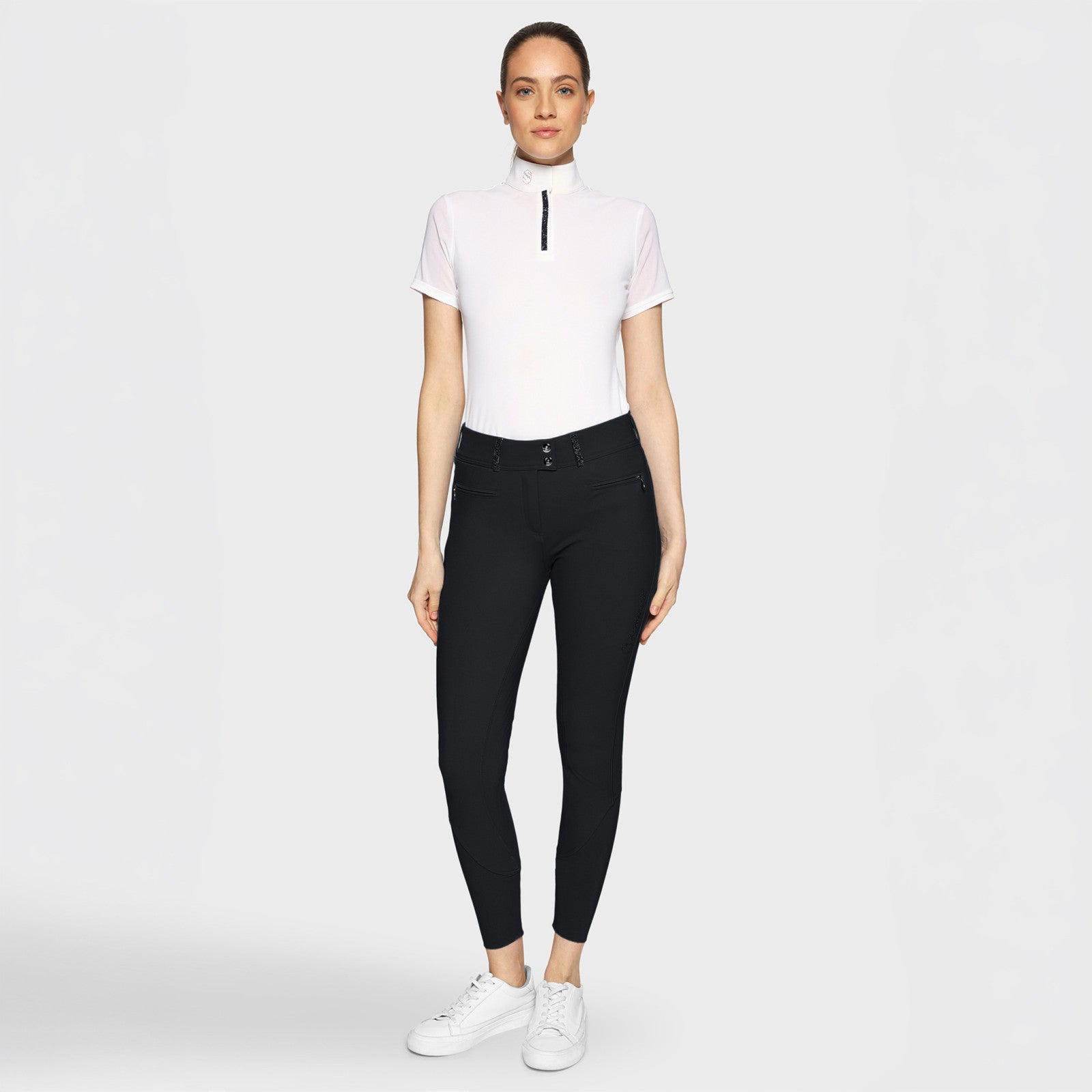 Full body front view of a female model wearing the black Samshield Clara Premium Full Grip Breeches with a white top on a plain background