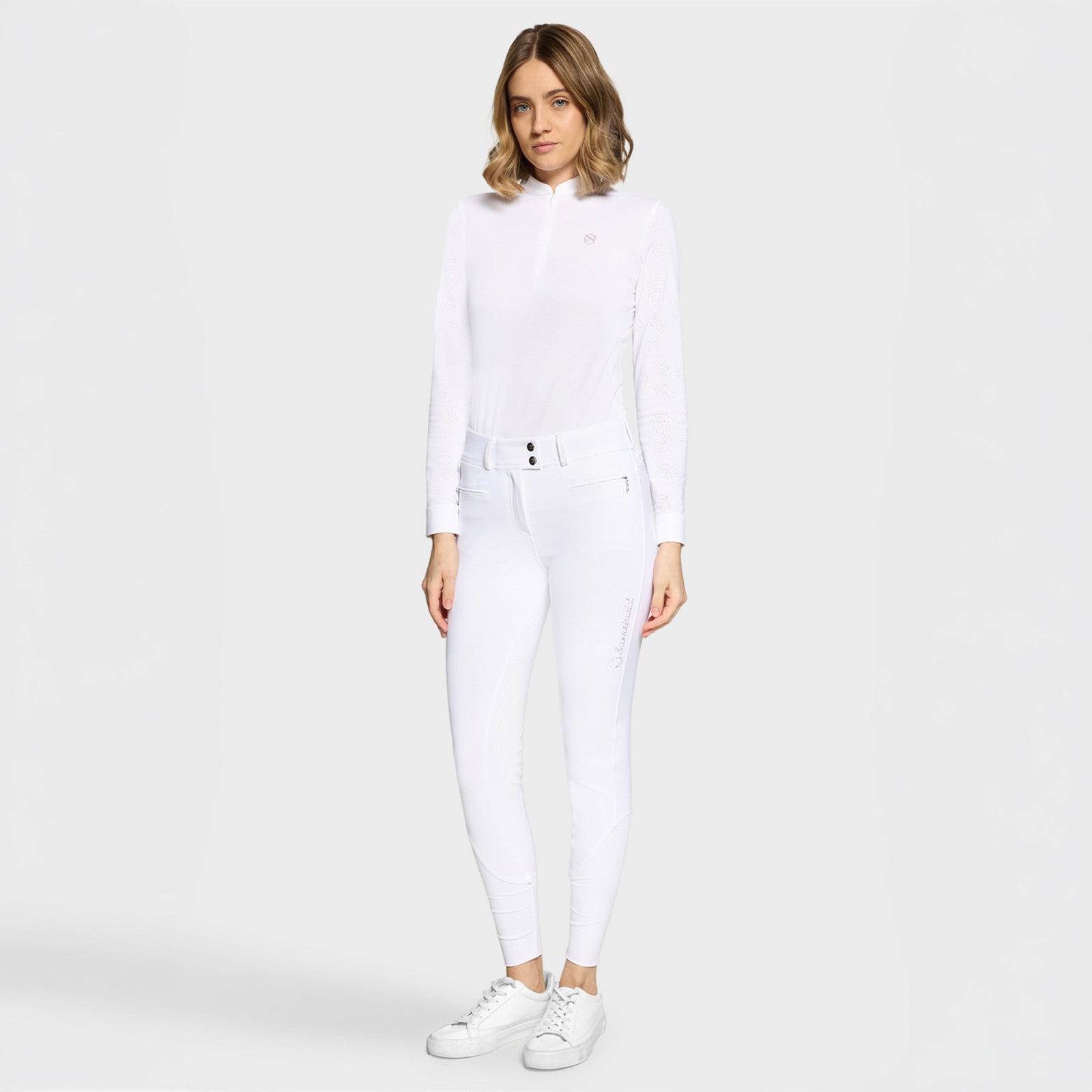 Full body front view of a female model wearing the white Samshield Clara Premium Full Grip Breeches and white top on a plain background