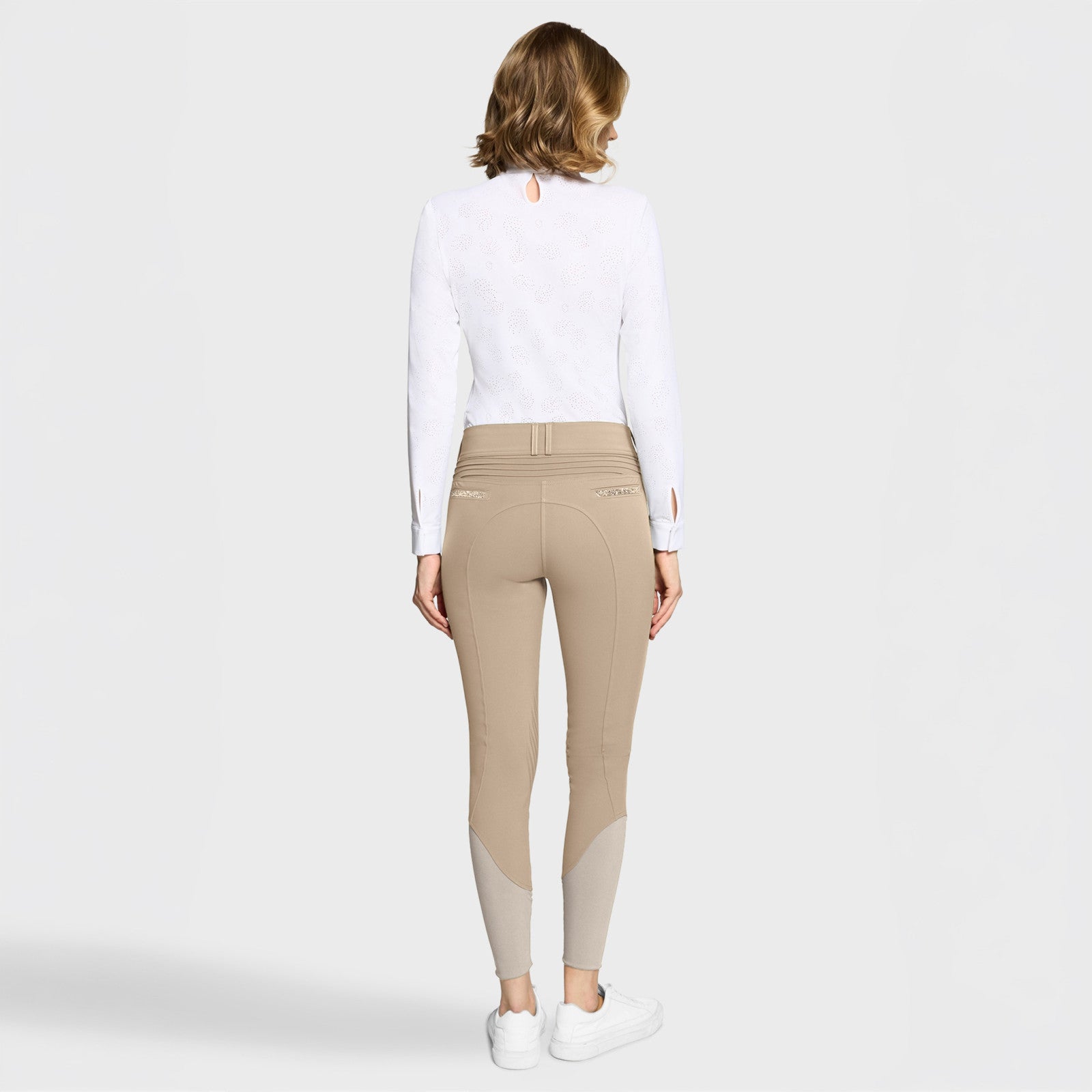 Full body back view of a female model wearing the sand Samshield Clara Premium Knee Grip Breeches and white shirts on a plain background