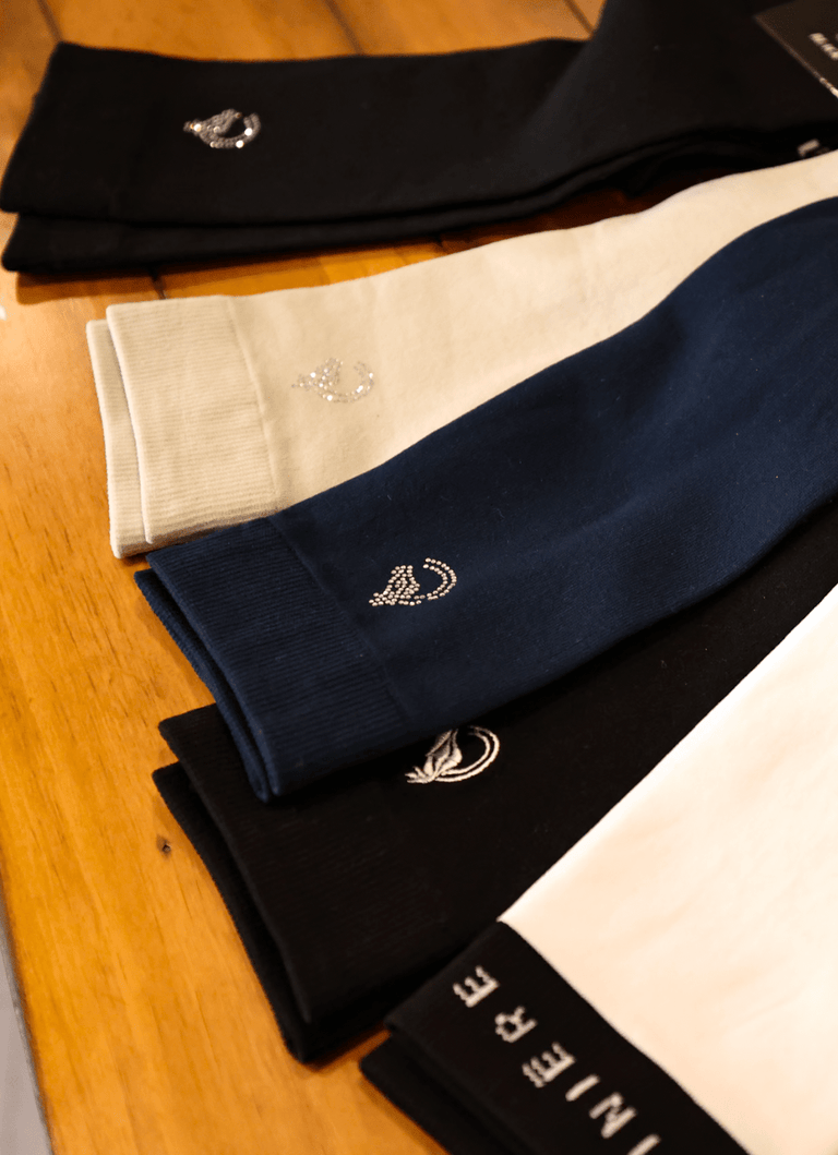 View of an assortment of colors of the Criniere Equestrian Socks lying on a wooden table