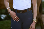 Front view of a model wearing the brown side of the Criniere Reversible Pebble Leather Logo Belt over navy breeches