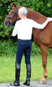 Back view of a male model wearing the navy KL Select Men's Evan Full Seat Breeches while petting a chestnut horse outside