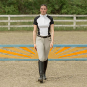 Front view of a woman wearing the Equinavia Sara Womens Perforated Short Sleeved Show Shirt in black and white while walking outdoors in a jump arean