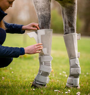 Person fastening Rambo Tech-Fit Fly Boot in silver on horse leg in grassy field