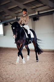 Angled front view of a female model riding a dark colored horse with a gold Equestrian Stockholm White Perfection Dressage Pad
