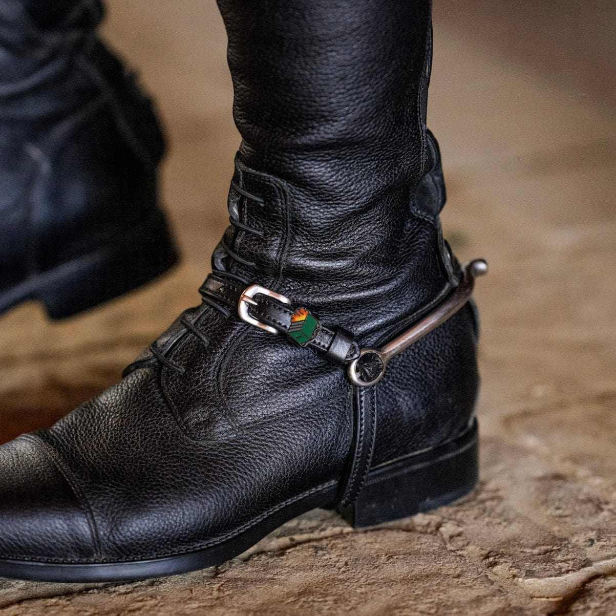 Close-up view of a Dumpster Fire Mane Jane Spur Strap over a black tall boot