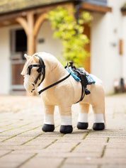 Angled front view of a palomino toy pony standing in front of a barn while wearing the black LeMieux Toy Pony Western Saddle